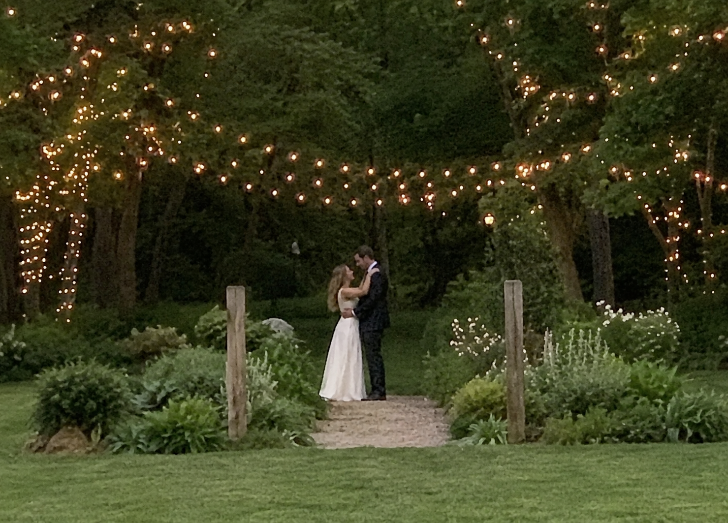 A couple dancing in a garden strung with fairy lights at dusk
