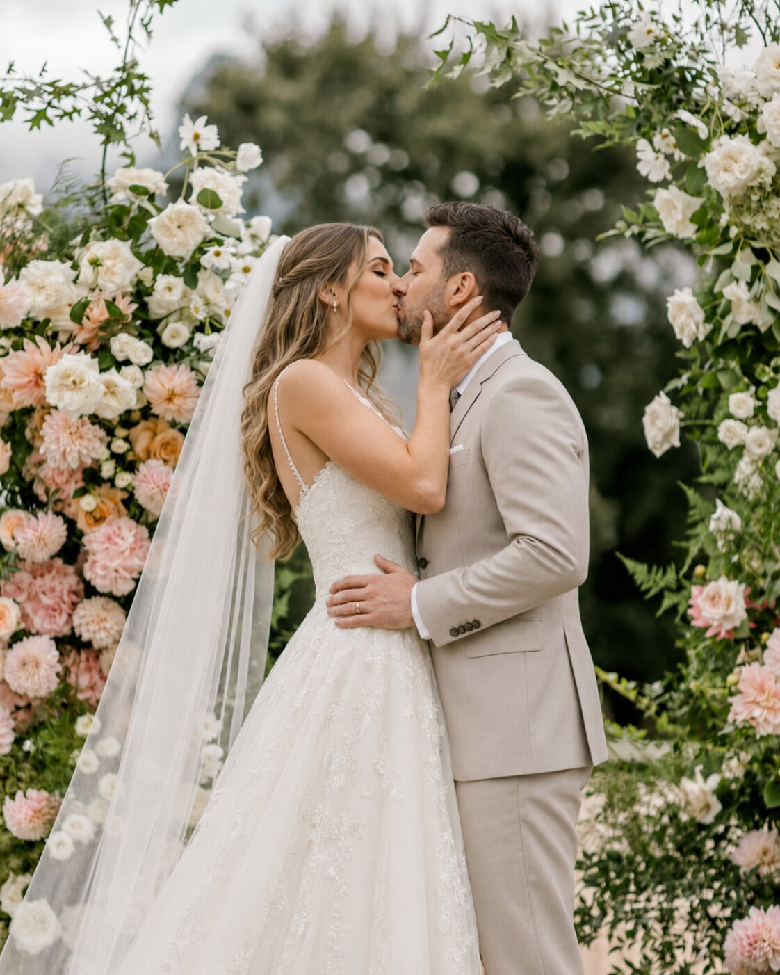 A couple's first kiss as newlyweds under a floral arch, soft golden light