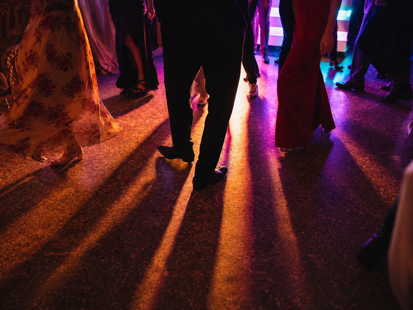 The dance floor late at night, warm and violet light, the couple mid-step among a blur of guests